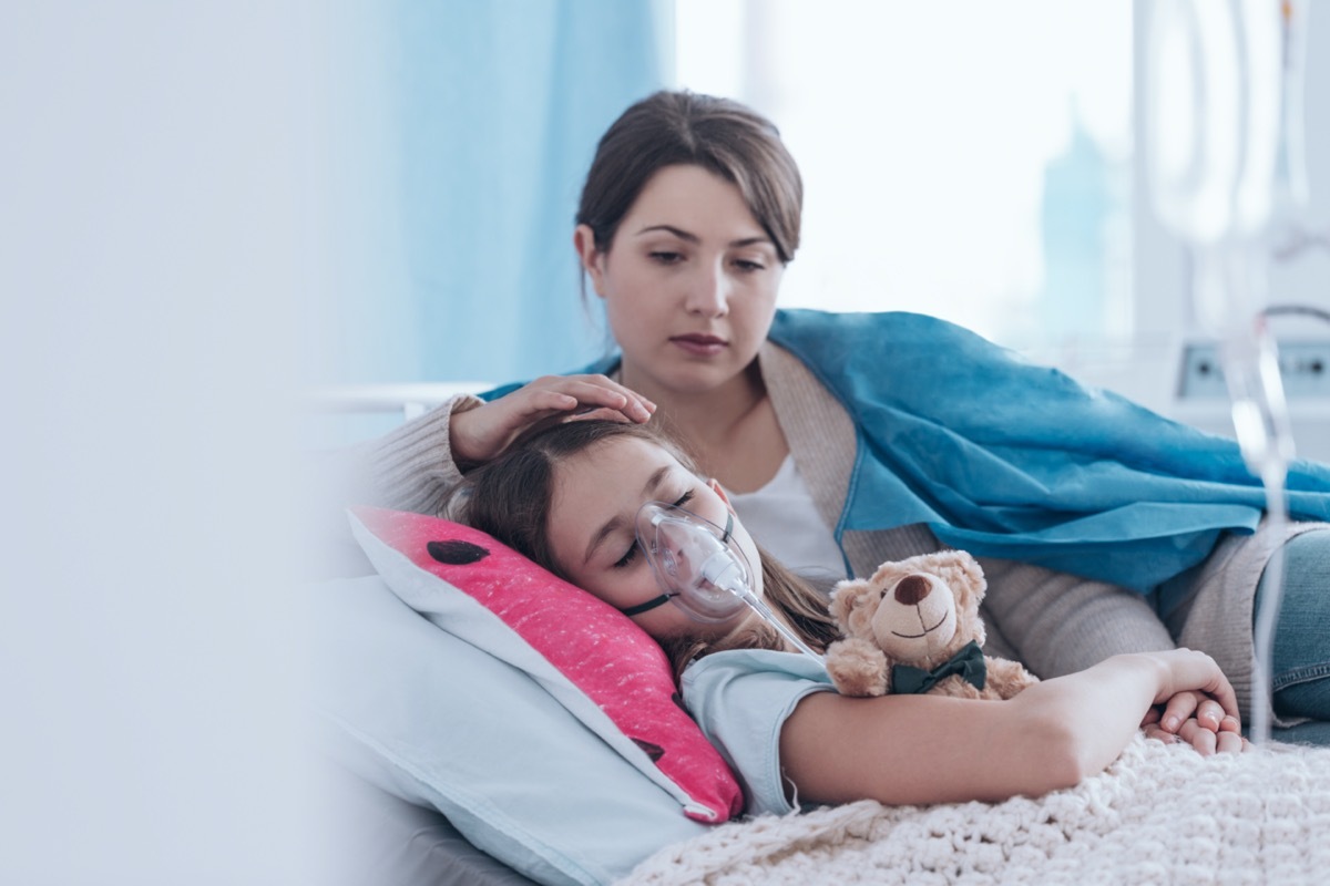 Worried mother taking care of a kid with cystic fibrosis lying in hospital bed with plush toy