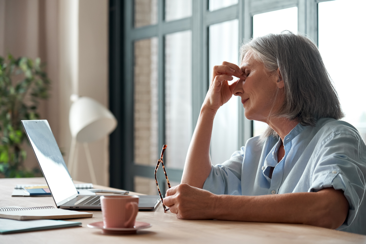 older white woman looking worn out sitting in front of her computer rubbing her eyes