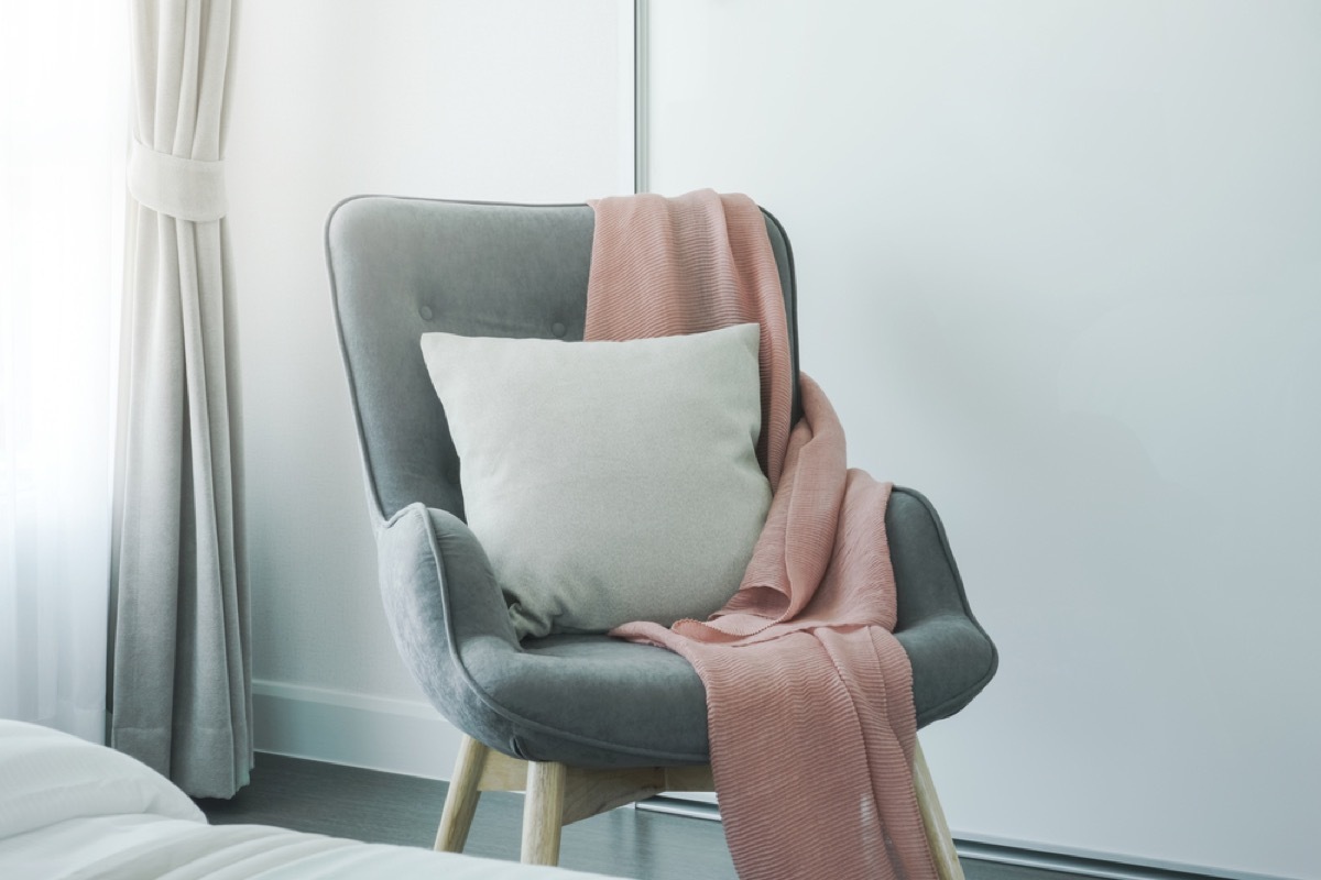 gray upholstered chair with pink blanket and white pillow