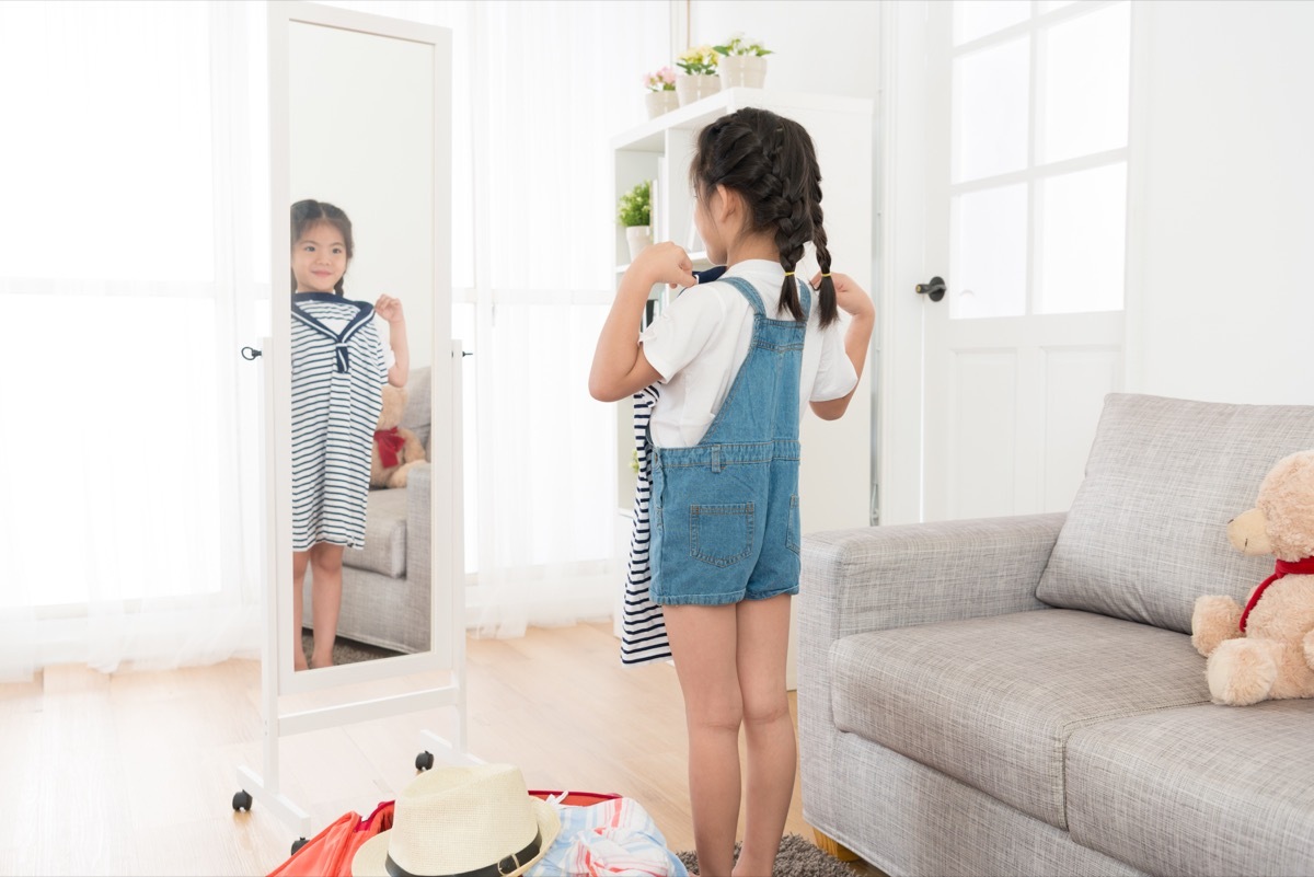 Little girl looking in the mirror at clothing options