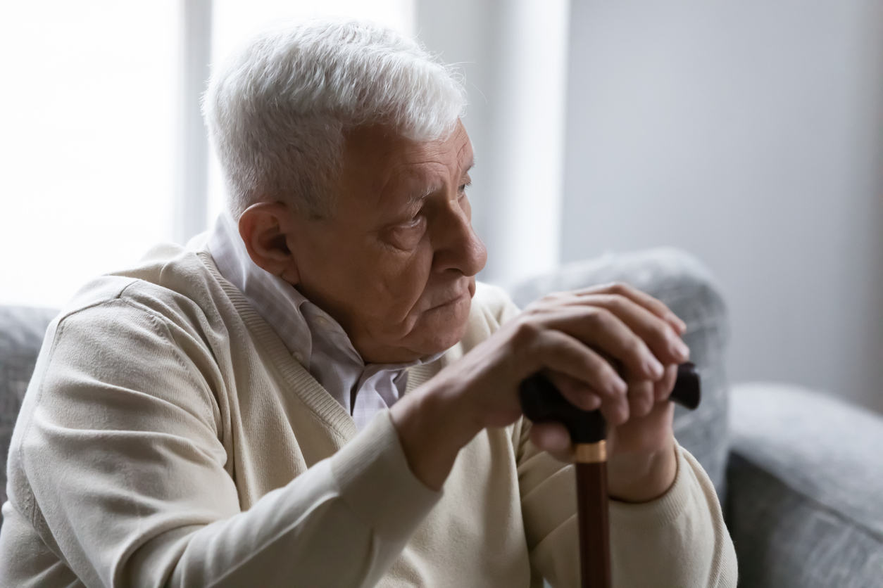 A senior man sitting on the couch and holding a cane