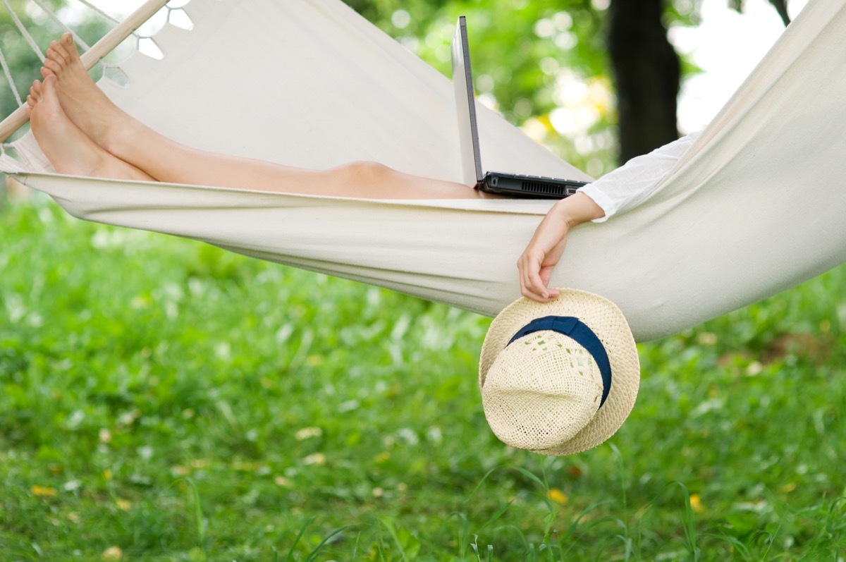 white woman relaxing outdoors in hammock with laptop