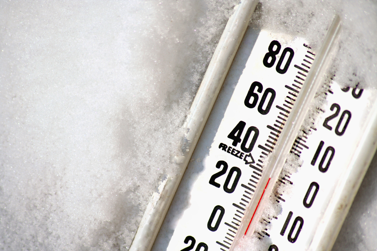 A close up of a thermometer resting in snow reading a low temperature