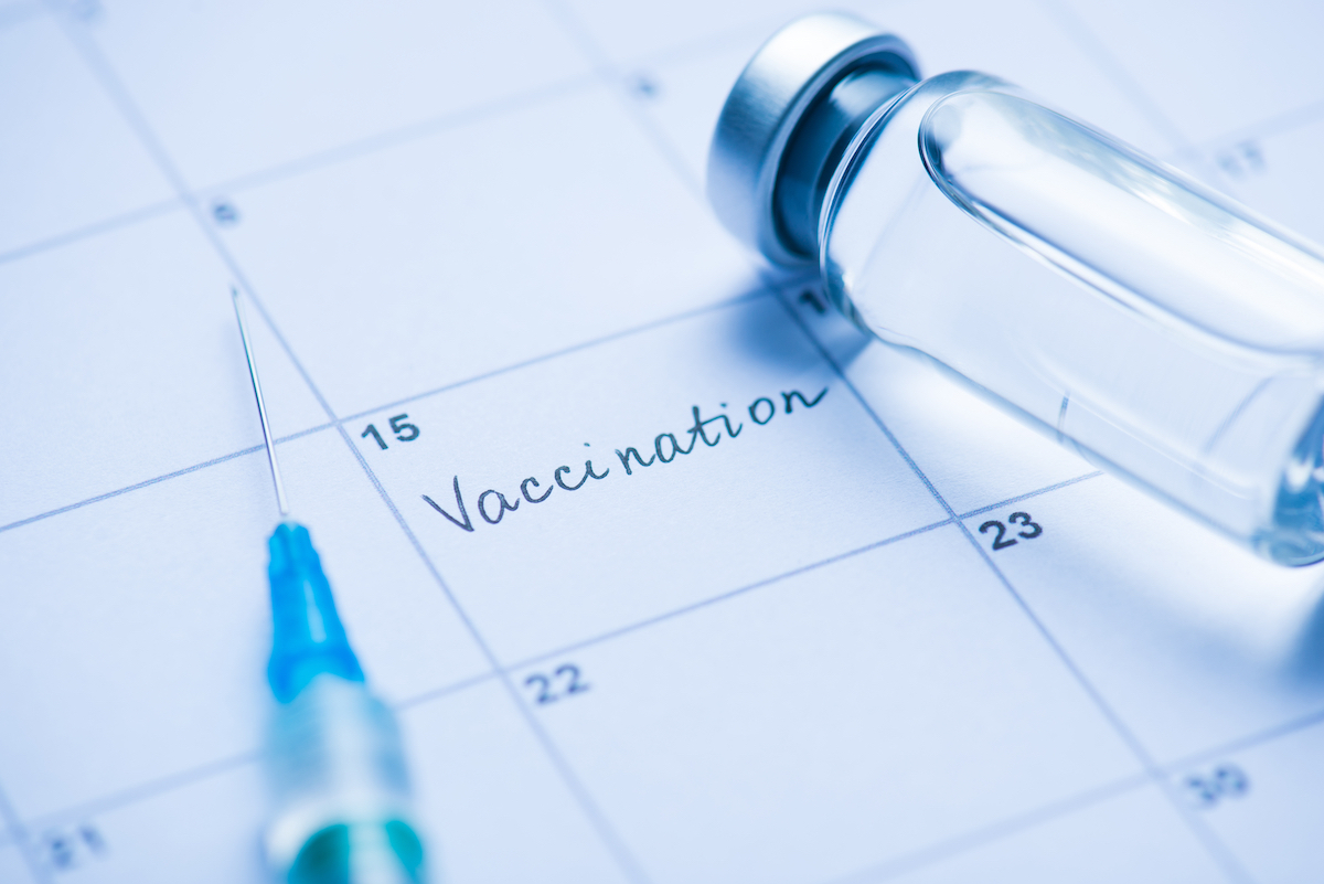 Close up photo of vial of a vaccine, syringe, and the word 