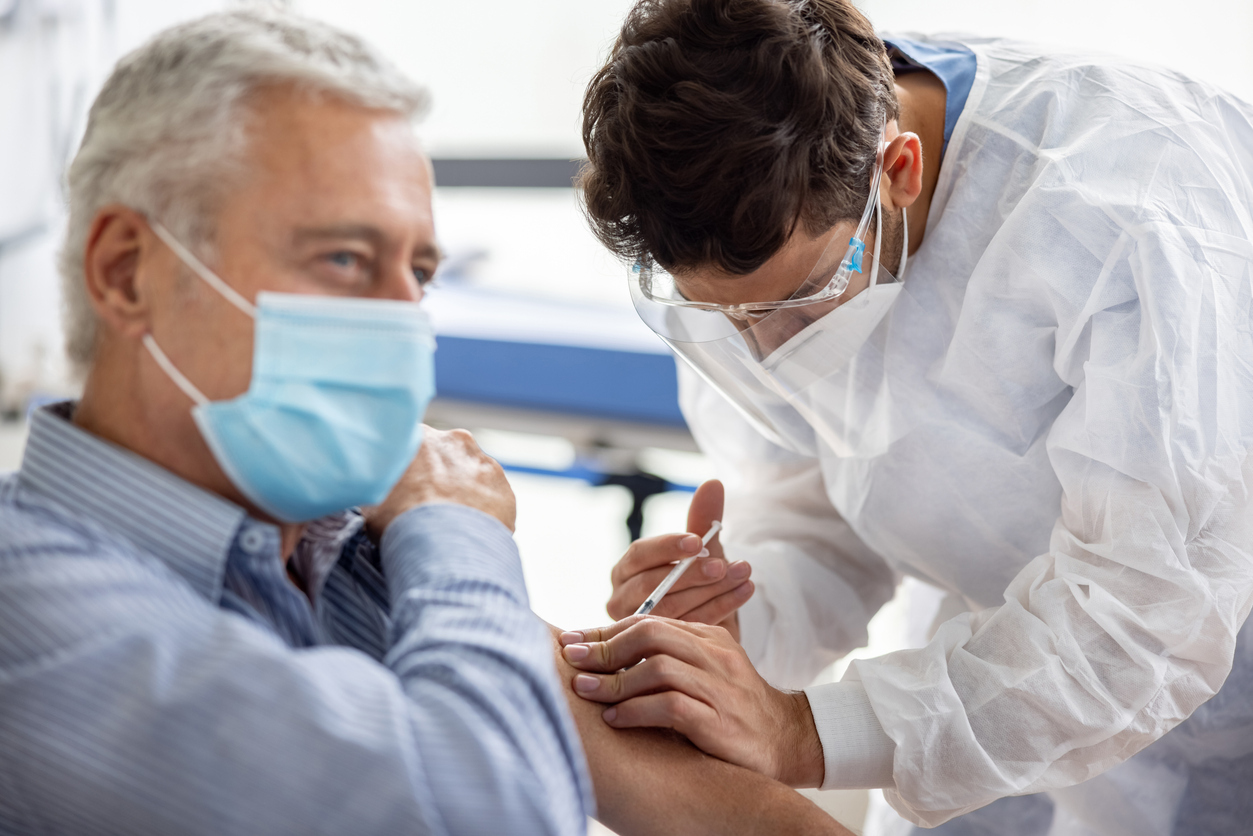 A senior man receiving a COVID-19 vaccine or booster shot from a healthcare worker