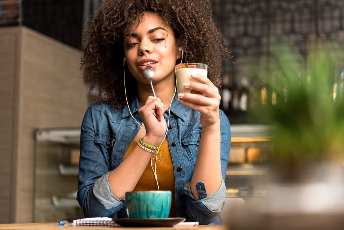 Woman listening to earphones while slowly eating a parfait in deep thought