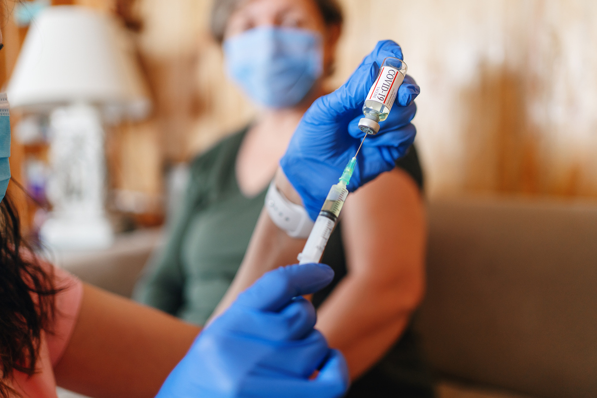 General practitioner vaccinating old patient at home