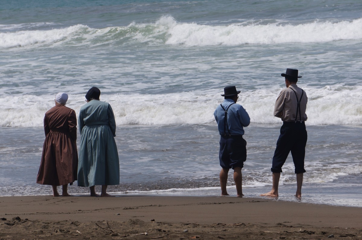 Four amish people standing on the sand in front of the beach