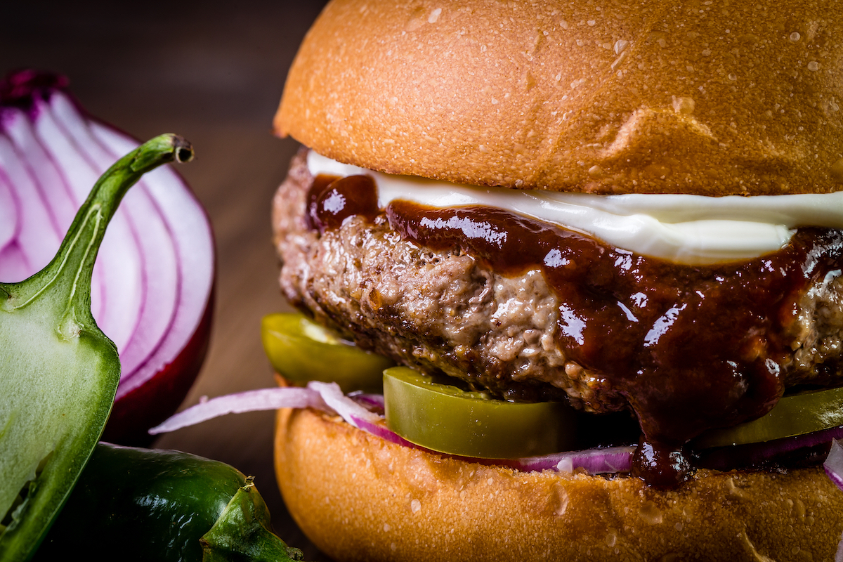 Craft beef burger with cheese, purple onion, jalapeno pepper on wood table 