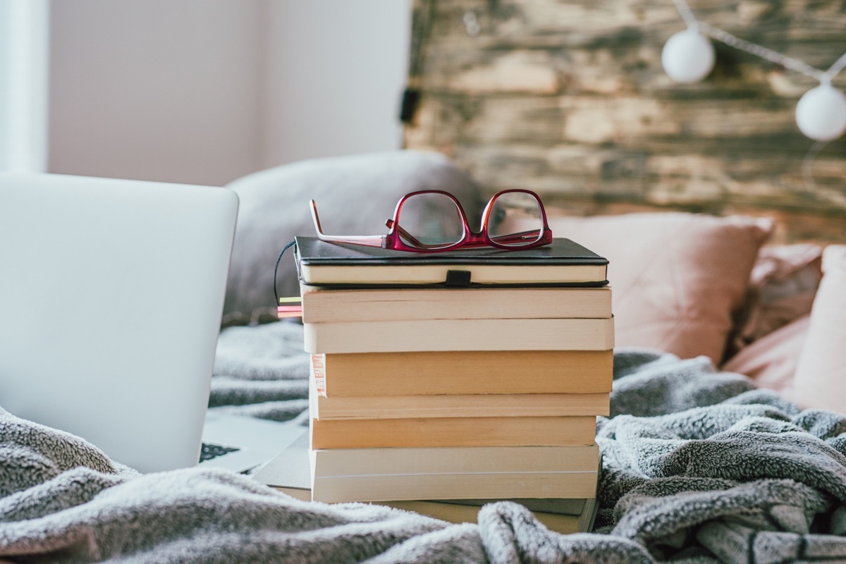 Shot of a pile of books with glasses and a laptop on the bed at home