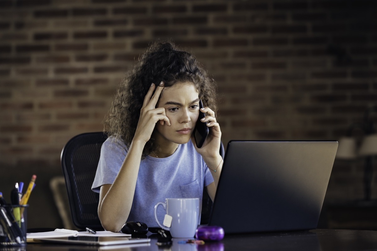 Working home: worried young woman using laptop and working at home office. Low key scene captured in a rustic kitchen.