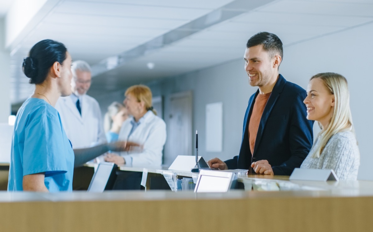 in the hospital at the reception desk nurse on Duty Answers young couple patients