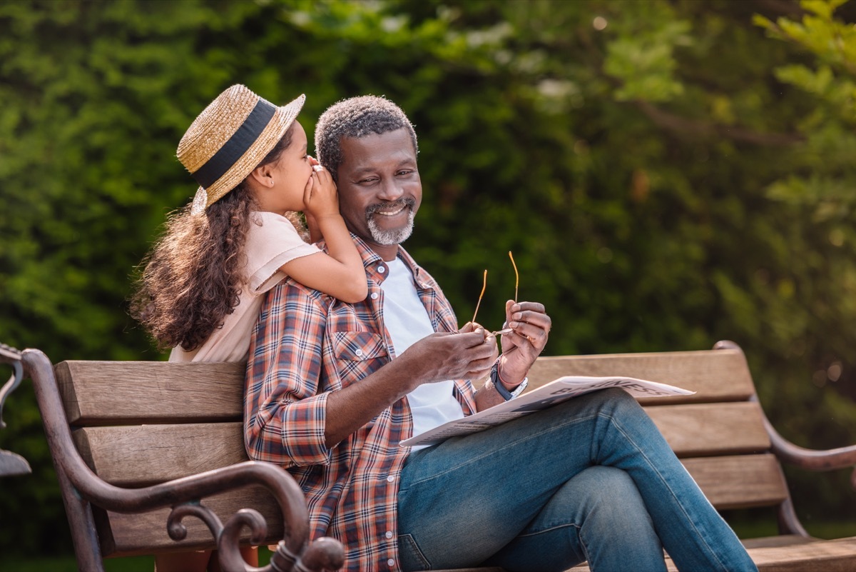 Granddaughter whispering secret to grandfather