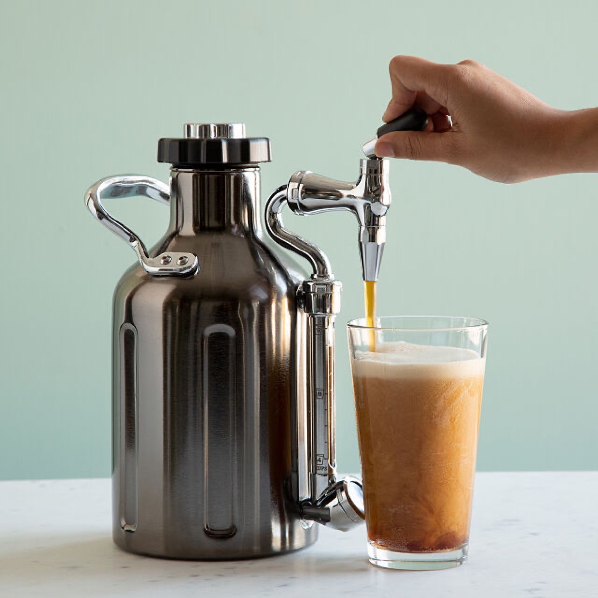 hand pouring coffee into glass out of silver device