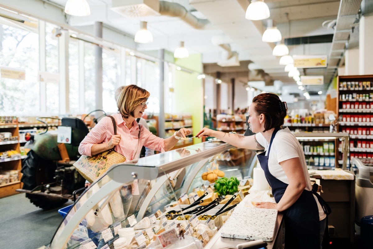 A mature woman tasting a cheese sample at the delicatessen at her local supermarket before making a purchase.