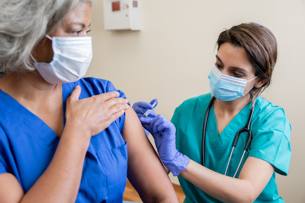 Nurse gives senior adult healthcare worker the Covid-19 vaccine