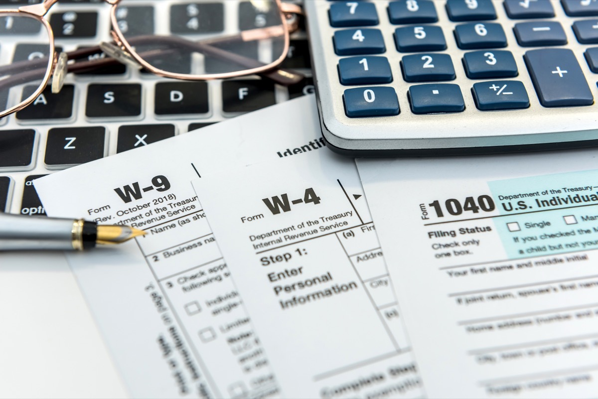 W-9, W-4, and 1040 form lying on desk with pen, glasses, laptop keyboard, and calculator