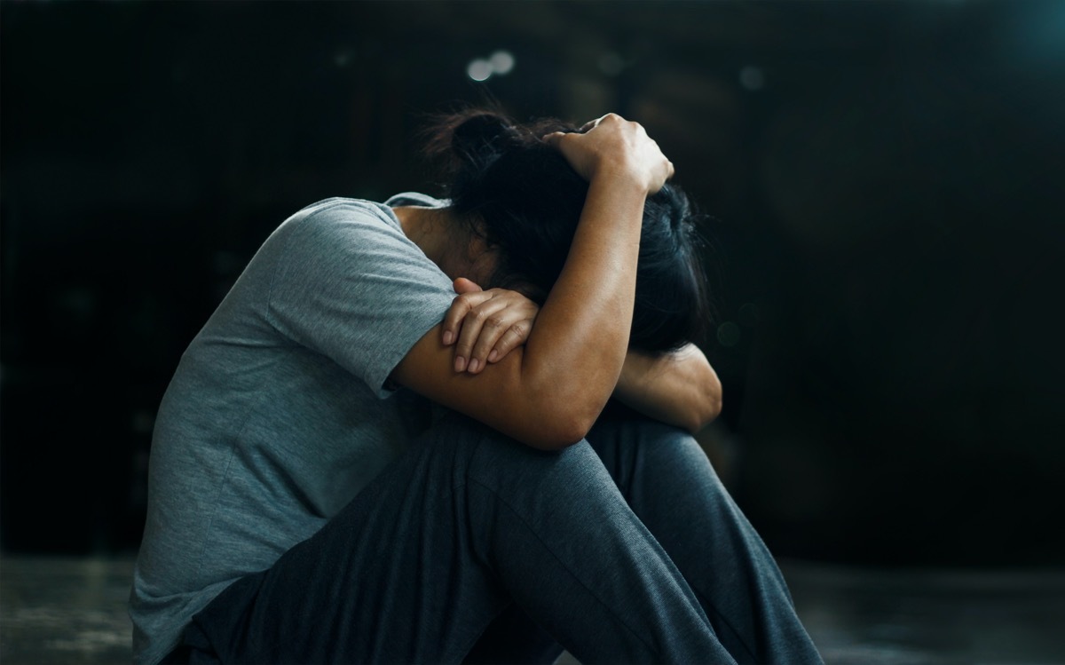 The depressed woman sitting alone on the floor in the dark room background