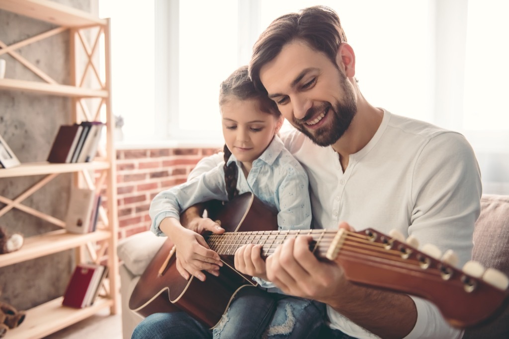 man holding young girl, teaching her to play guitar