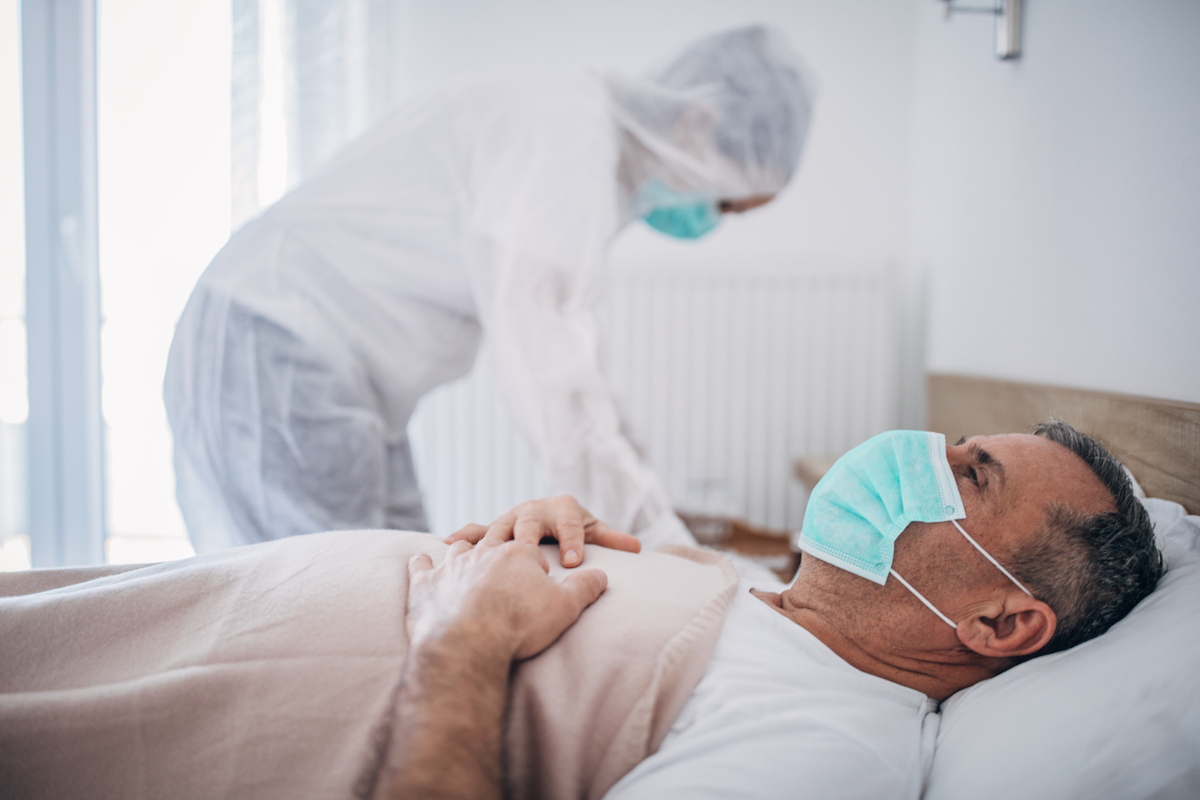 Man lying in hospital bed because of coronavirus infection, doctor is standing next to him.