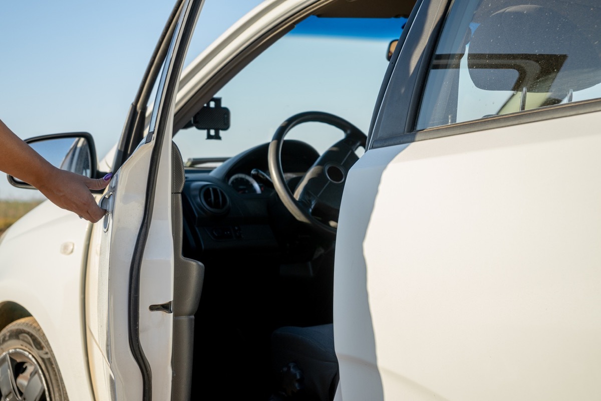 Woman hand opening the door of a white car casting a shadow over it at sunrise time