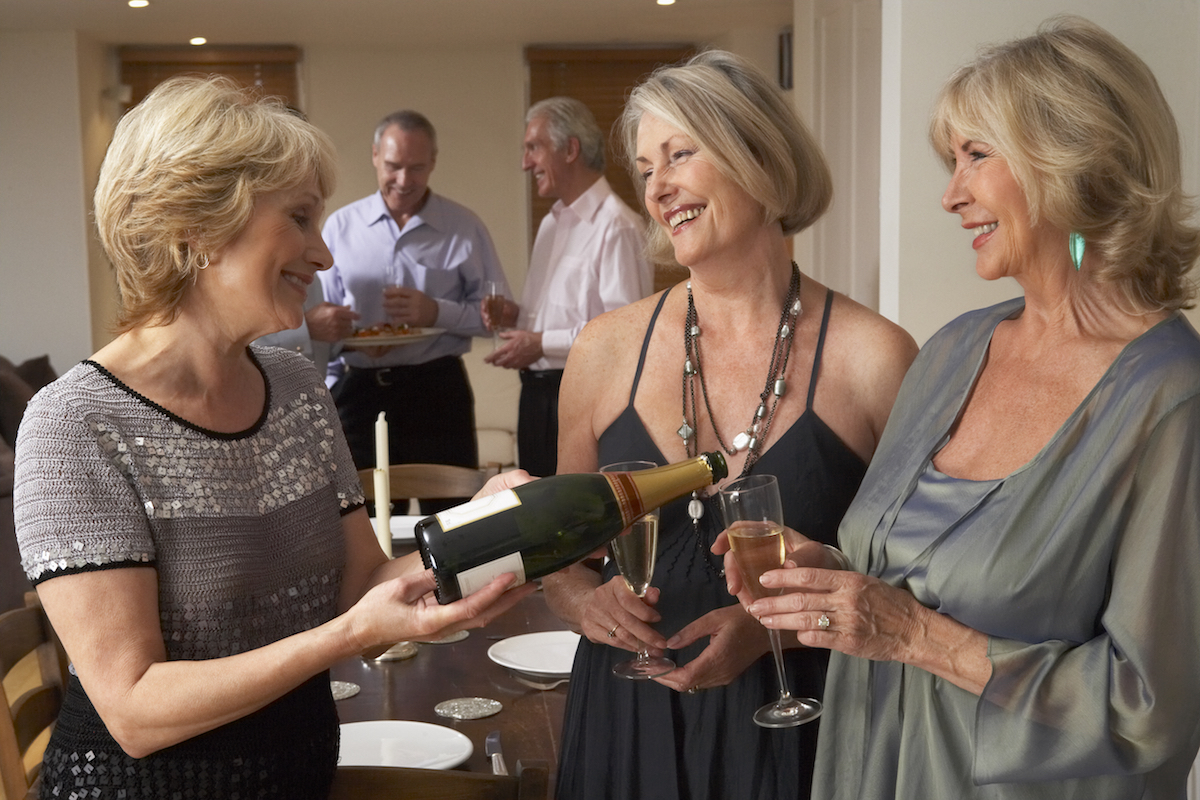 Woman Serving Champagne To Her Guests At A Dinner Party