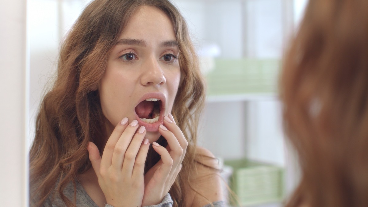 Young woman looking inside her mouth in a mirror