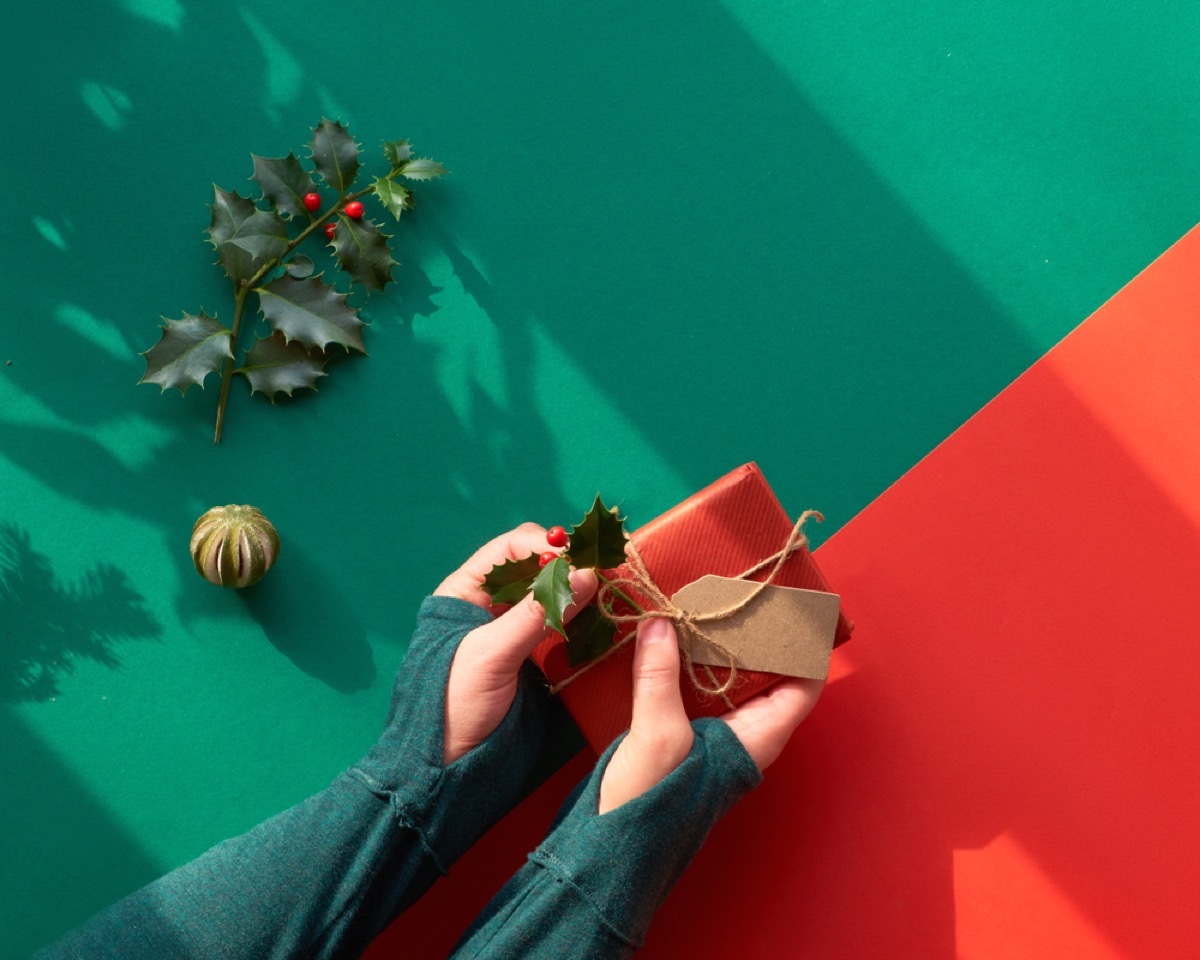 woman wrapping present in brown paper and attaching holly leaves and berries