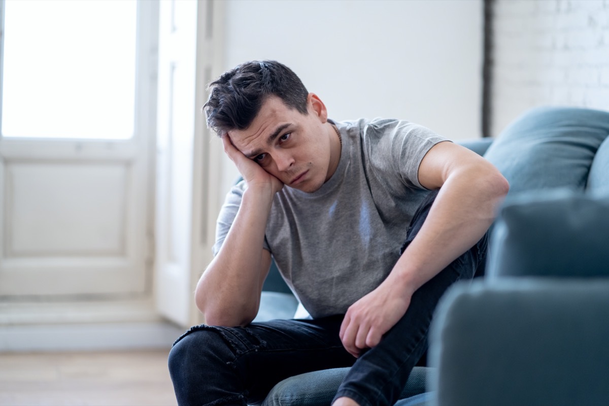 Portrait of young man felling depressed and desperate crying alone in sofa home suffering emotional pain and unhappiness