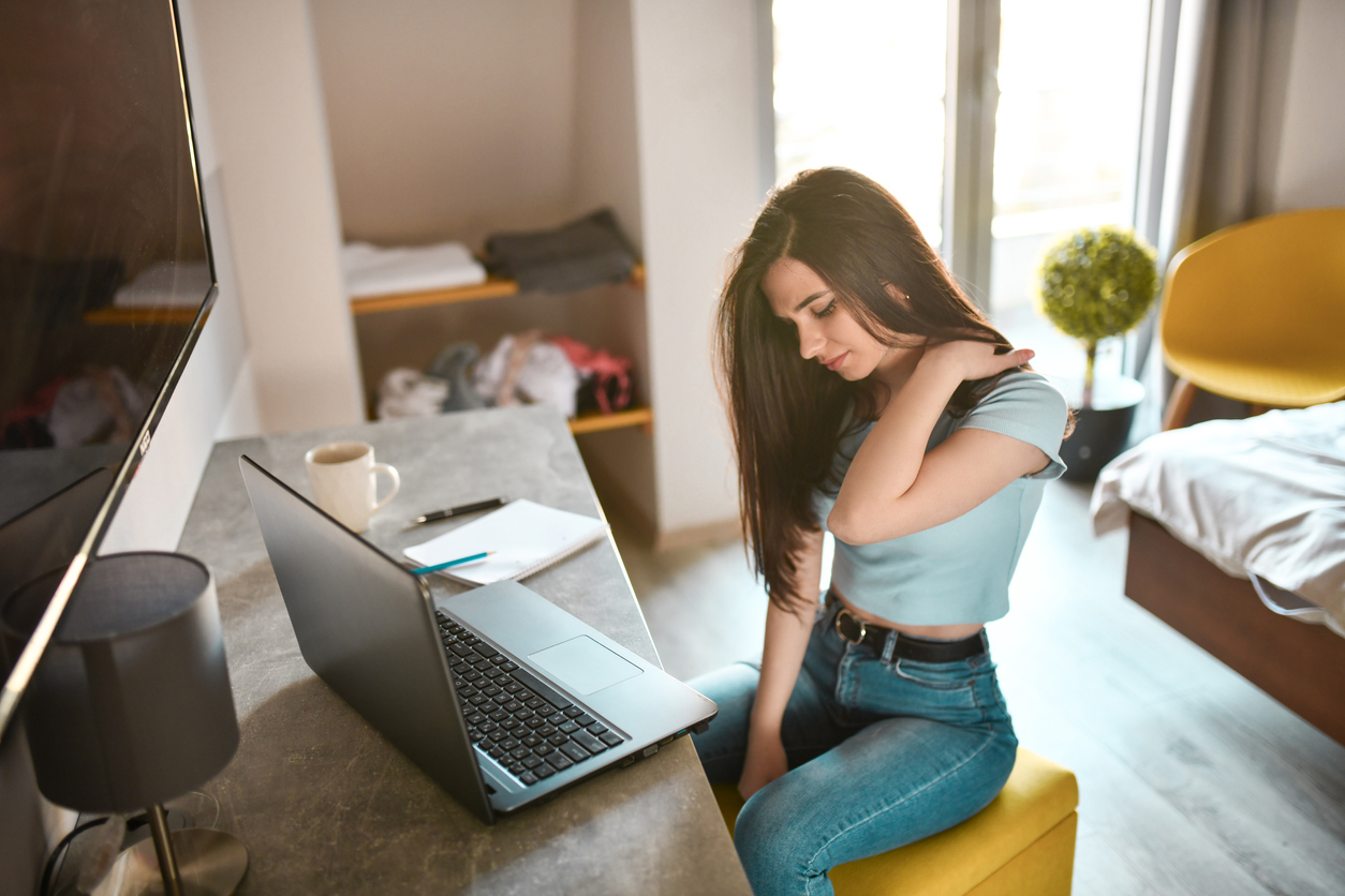 Woman sitting with laptop rubbing her shoulder.