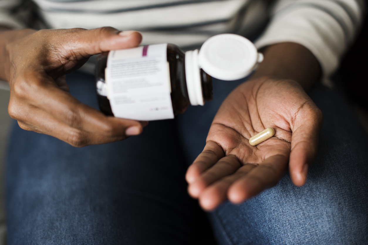 A closeup of a hand holding a supplement pill out of the bottle