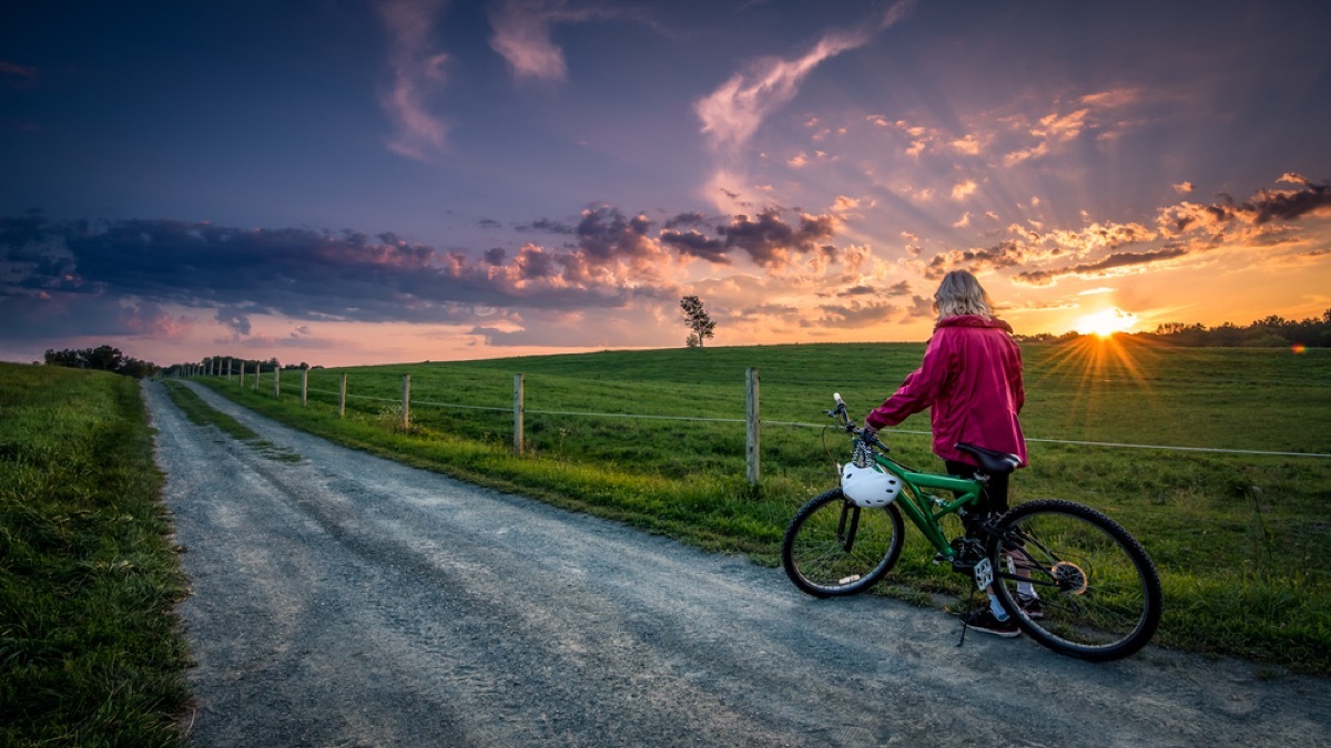 older woman with bike on a country road at sunrise