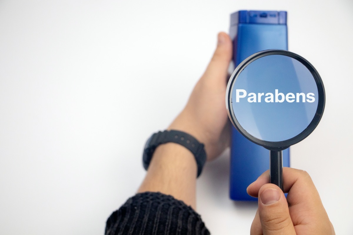 A hand holds a blue jar and a magnifier, where the harmful ingredients of a detergent are written in close up.