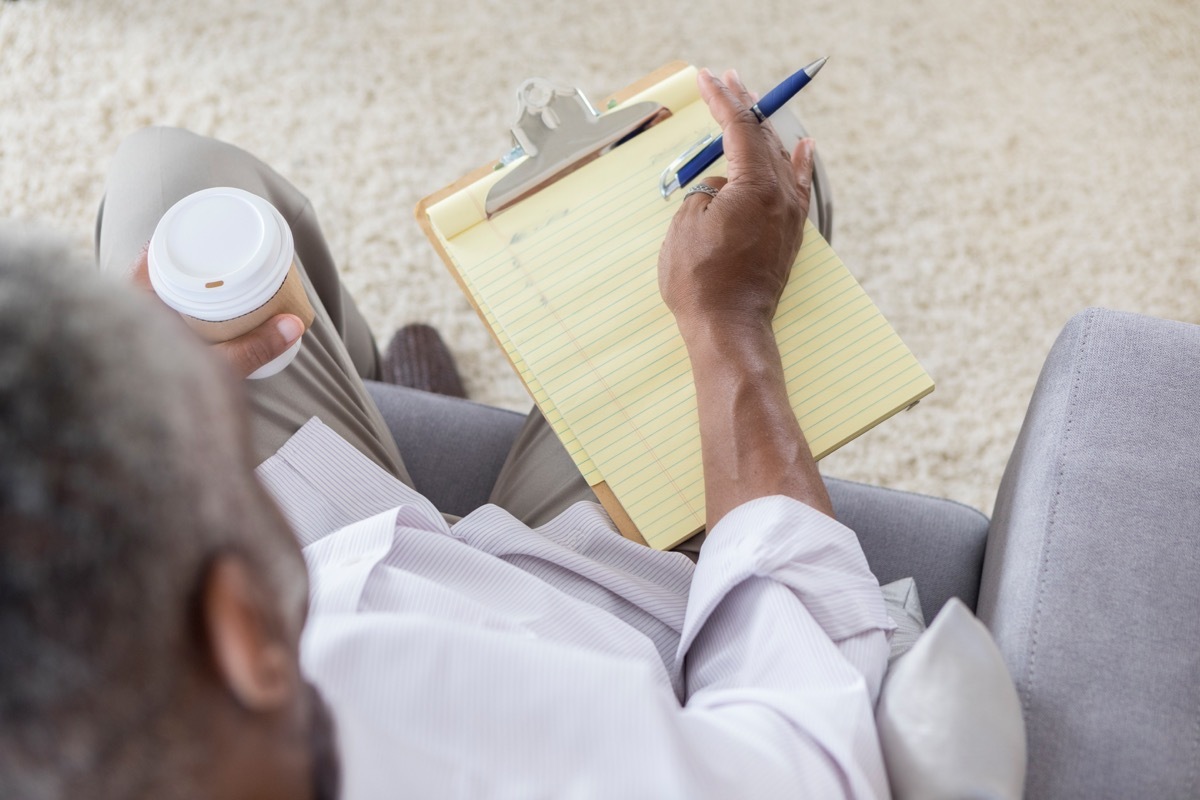 man writing his list of goals down while holding to go coffee cup