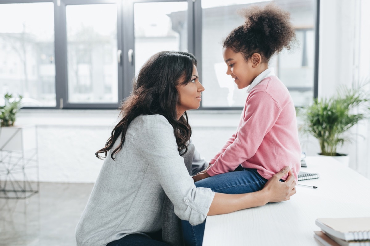 mother crouched down talking to daughter sitting on table, prepare children for divorce