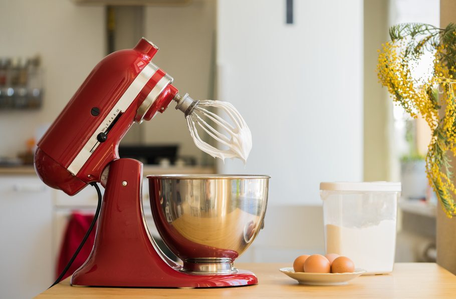 A red KitchenAid stand mixer in the up position with a bowl below the whisk