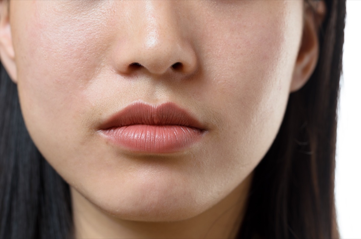 Cropped view of the lower facial features and closed mouth of a young woman with a serene calm expression and long dark hair