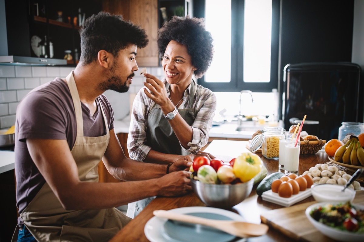 Beautiful young couple having fun and laughing while cooking in kitchen at home