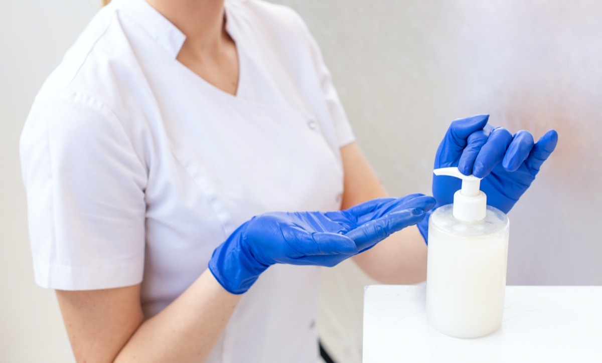 Hands of a woman in a blue protective glove cleaning hands with a bacterial gel for viral hygiene