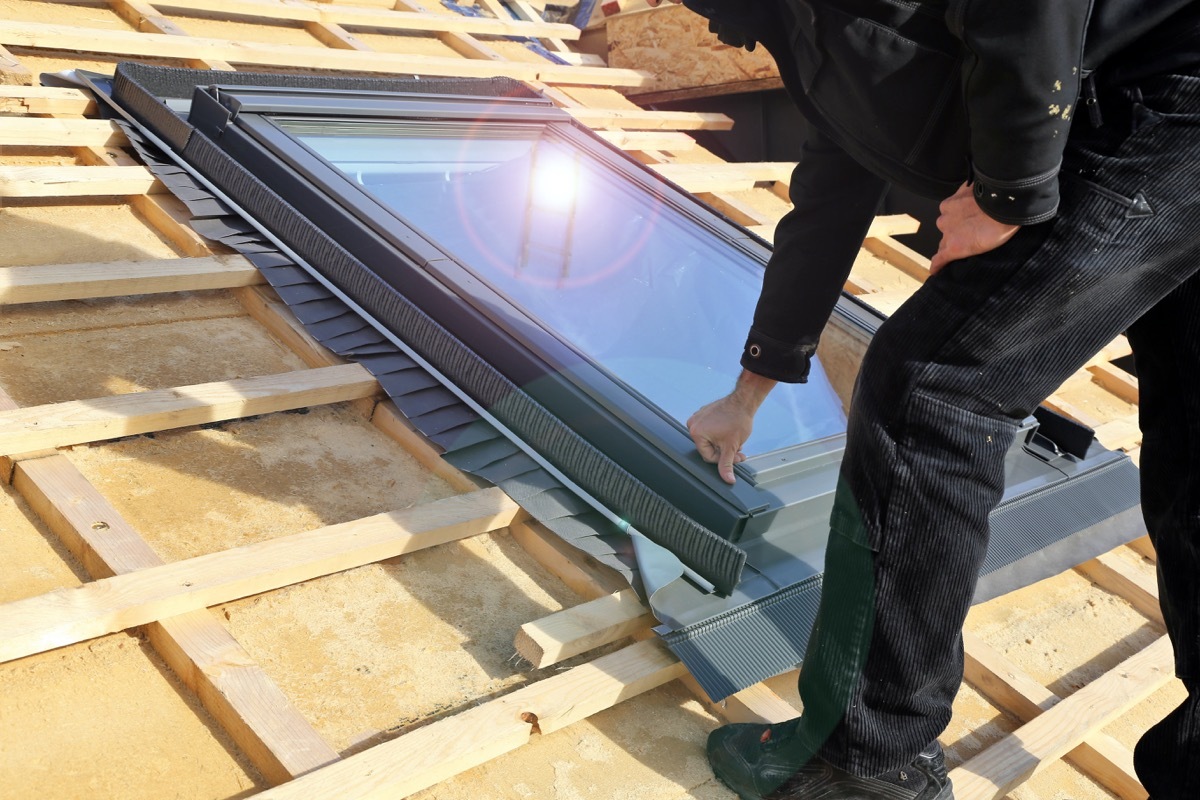 white man in black clothing installing a skylight on roof