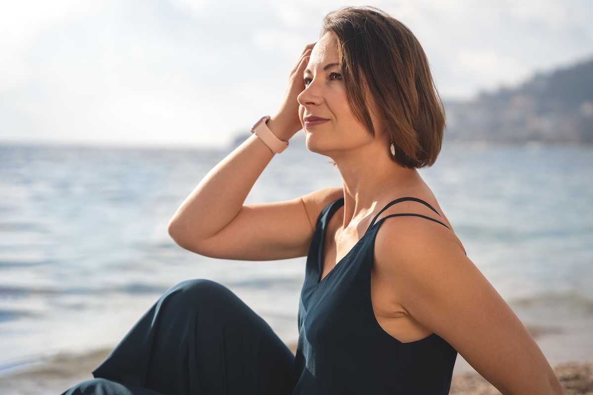 A middle-aged woman sitting on the beach wearing a black dress.