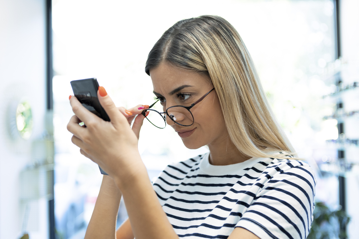 Redhead young woman with eyesight problems trying to read phone text