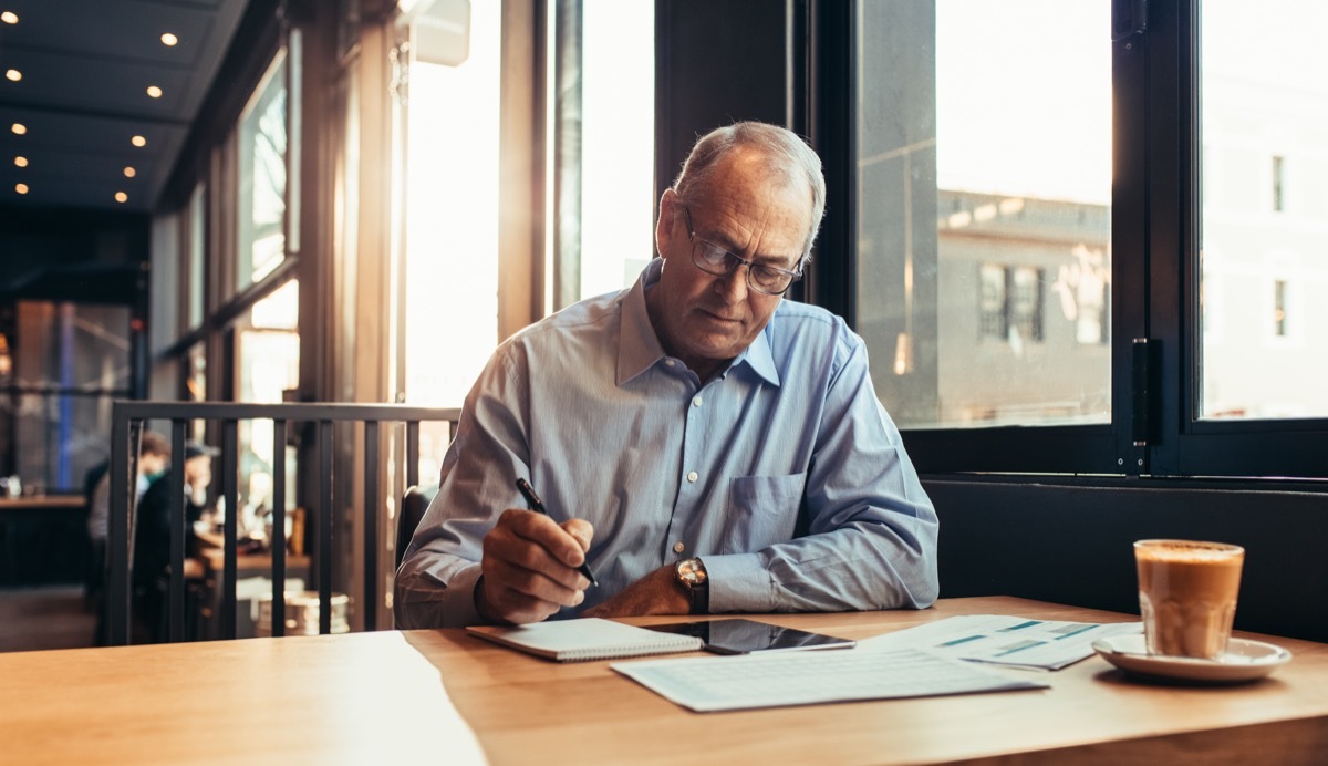 Mature businessman making notes while sitting at cafe. Senior man at modern coffee shop working.