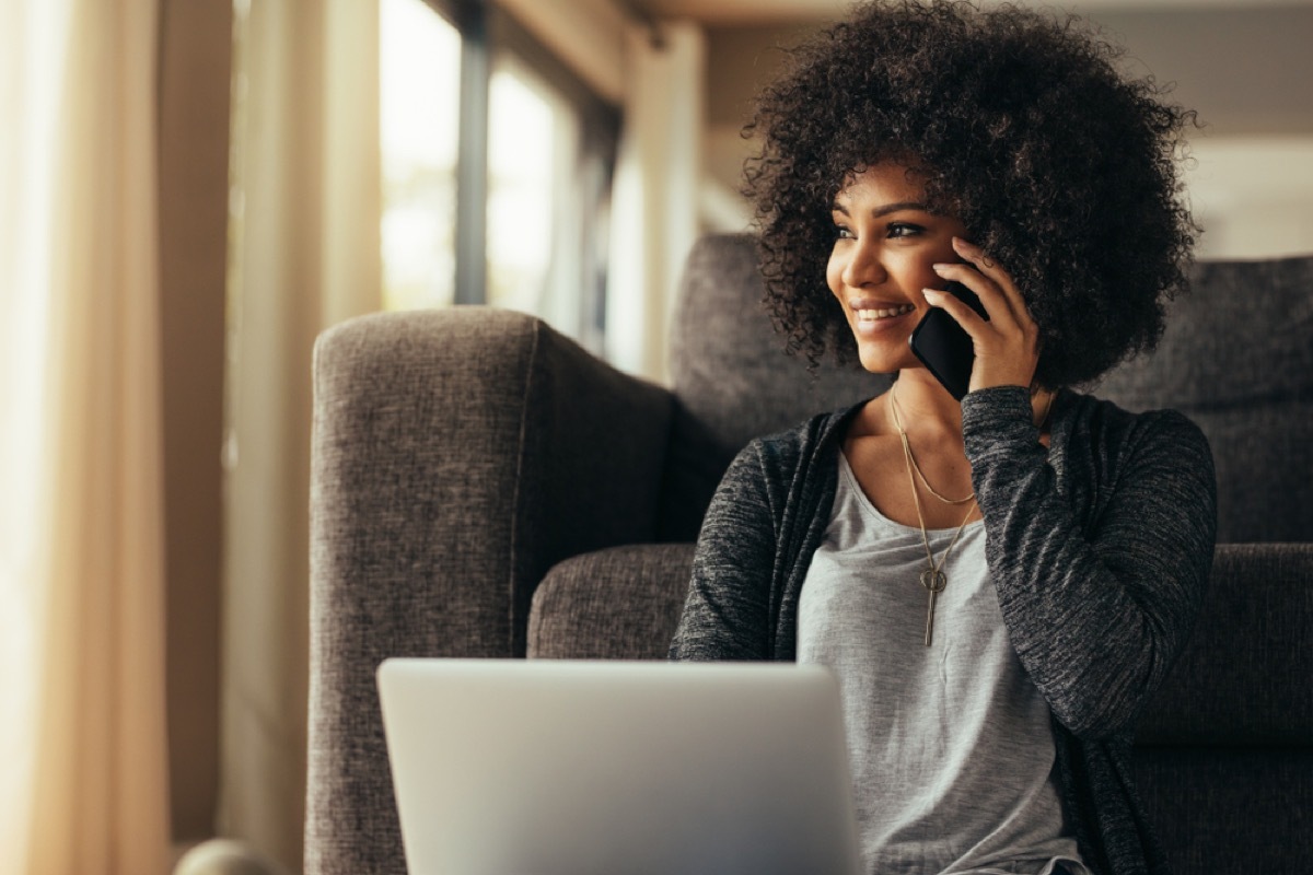 black woman smiling while on the phone in front of her laptop