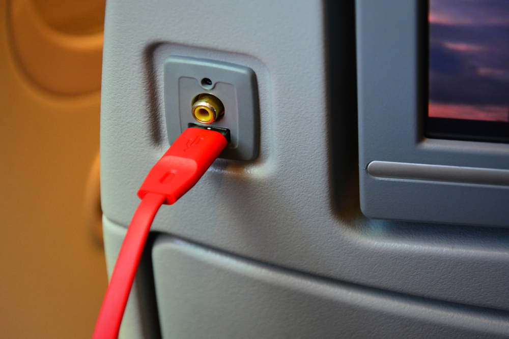 A USB charger and power outlet plug on the back of a seat on a plane