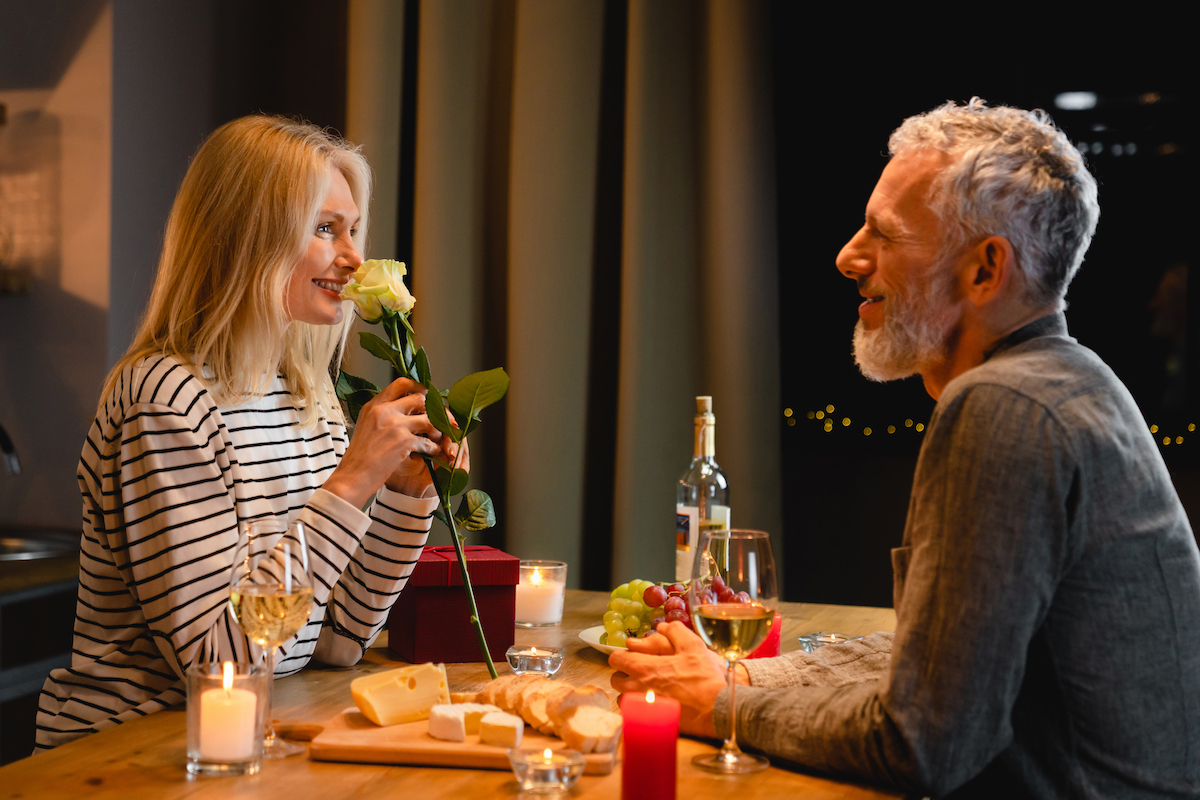 A happy couple in their 50s enjoying a dinner date; the woman is smelling a rose