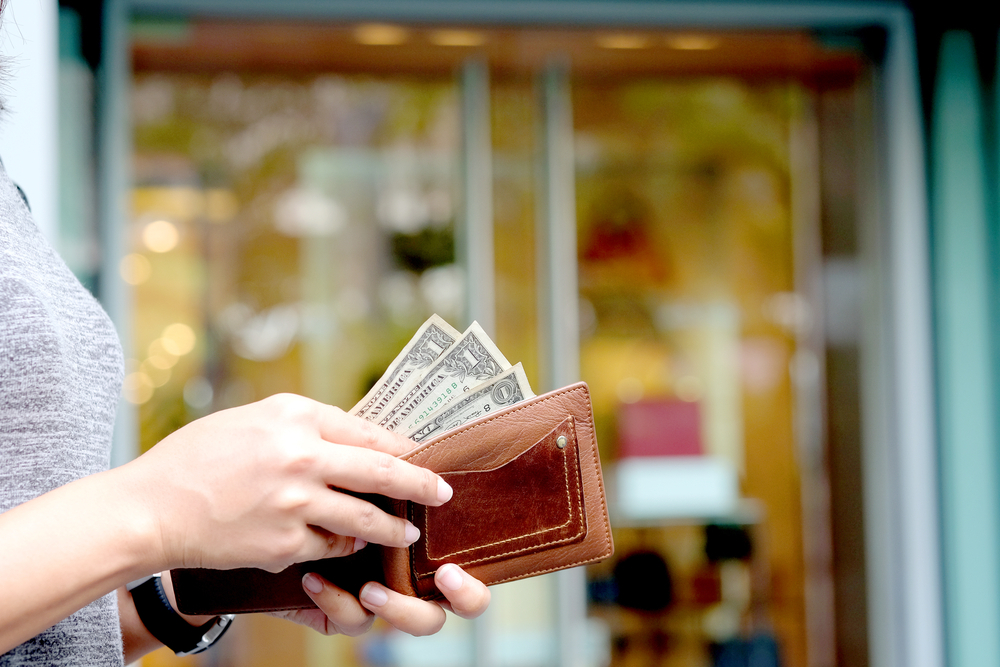 A close up of a person taking three dollar bills out of their wallet