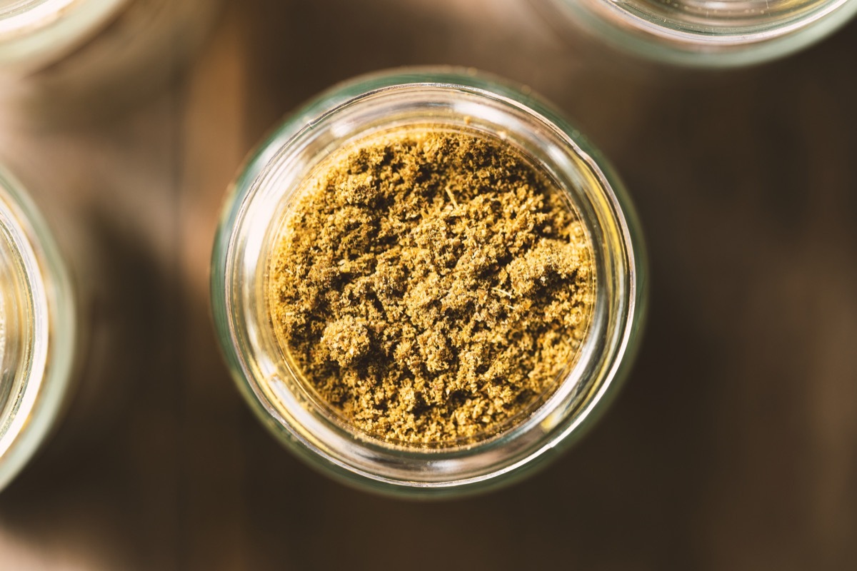 Cumin in glass jar on rustic wooden background. Spices from directly above, selective focus.