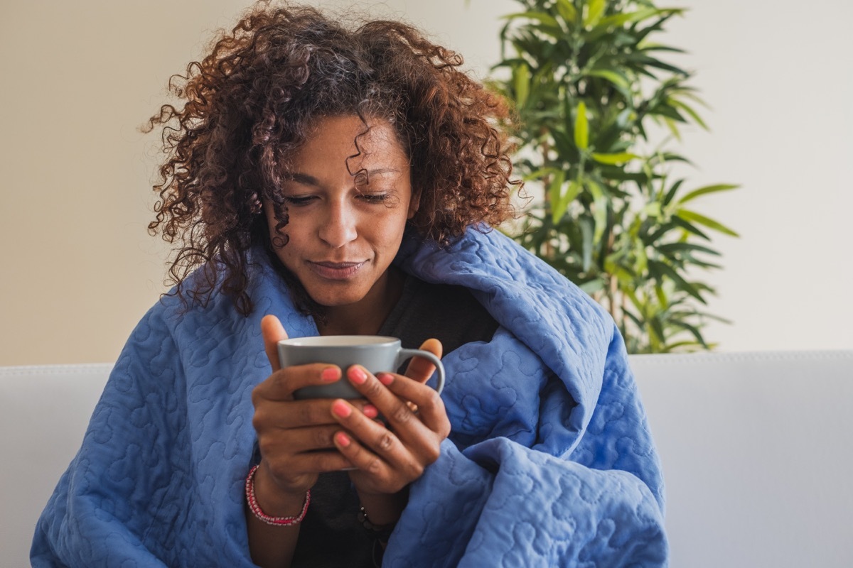 Cold woman warming up with a cup of coffee and a blanket