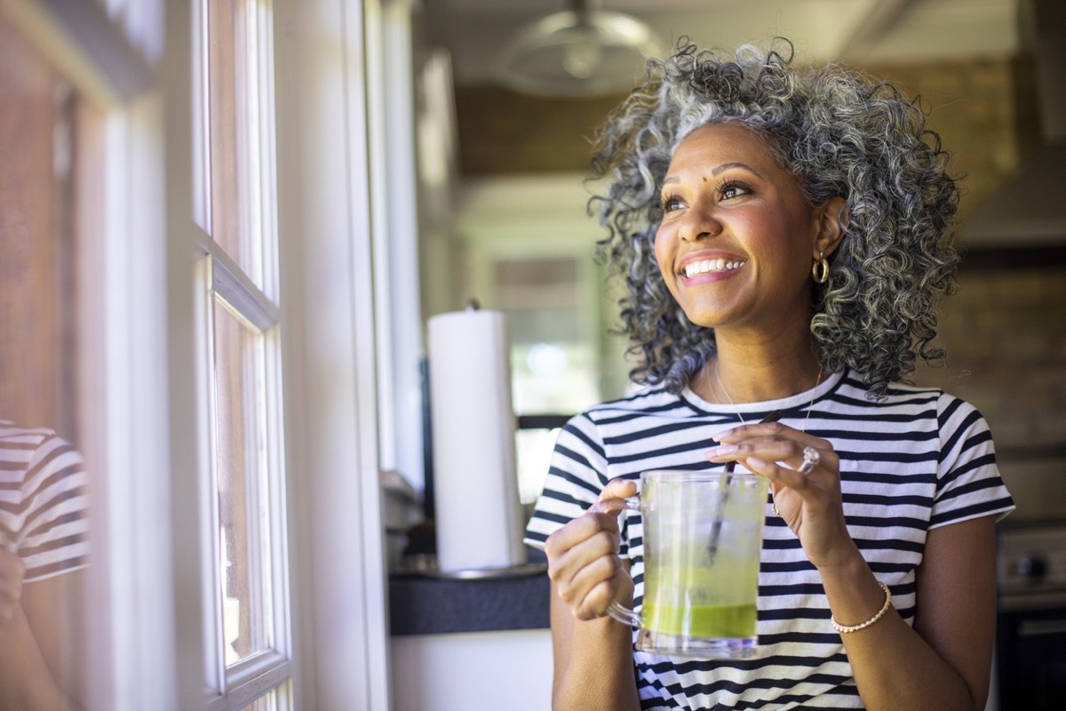 middle aged black woman with white curly hair drinks a green smoothie in the morning for breakfast